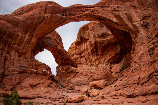 View of the iconic Double Arch natural sandstone formation in Arches National Park, featuring massive red rock arches against a cloudy sky in Grand County, Utah, United States.