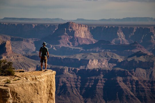 View of a man standing on the edge of a cliff overlooking the vast rugged rock formations of the Grand Canyon in Coconino County, Arizona, United States.