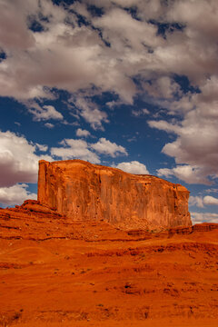View of the iconic red sandstone butte in Monument Valley under a bright blue sky with scattered white clouds in Oljato-Monument Valley, Arizona, United States.