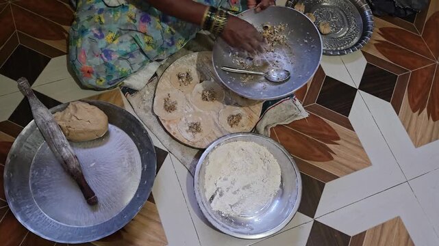 A woman filling jaggery coconut stuffing into rolled dough puris on a wooden board before expertly hand-pleating authentic ukdiche modak dumplings for a Maharashtrian festival celebration.
