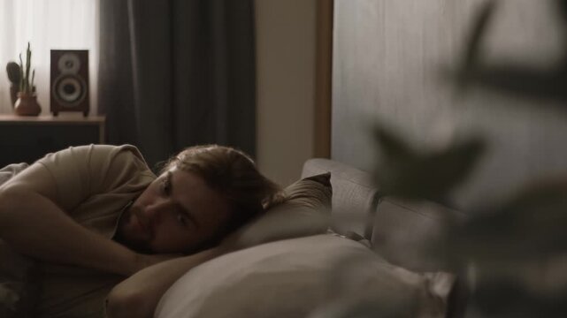 Young adult Caucasian man waking up in bedroom, turning over and resting thoughtfully in bed. Perfect for sleep disorder awareness and morning healthcare ads
