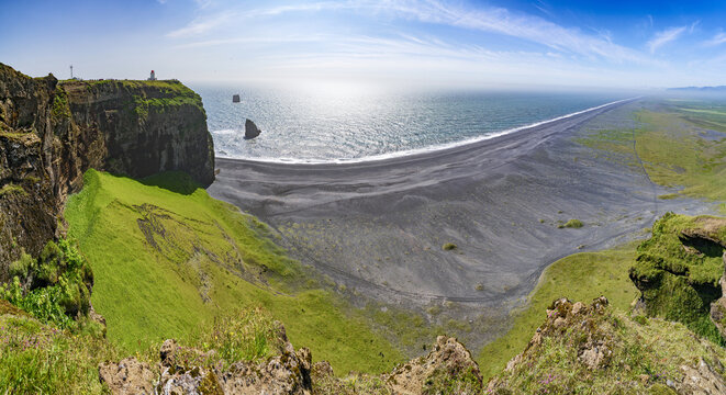 View of the dramatic Dyrholaey cliffs with lush green grass overlooking the expansive black volcanic sand beach and the Atlantic ocean in Vik, Myrdalshreppur, Iceland.