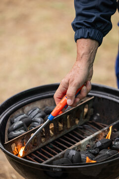 mano di uomo adulto caucasico che accende il fuoco con un accendino in un barbeque per preparare una grigliata all'aperto, in estate