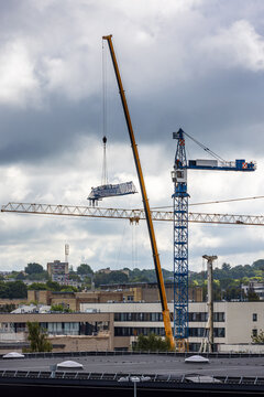 View of a mobile crane lifting a steel truss component at a construction site with a tower crane and urban buildings in the background in Vilnius, Vilnius County, Lithuania.