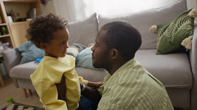 African American father hugging and talking with young son at home in slow motion. Perfect for parenting campaigns, life insurance ads and family wellbeing promos