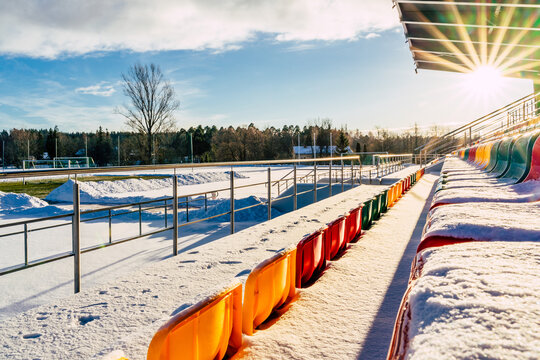 View of colorful stadium seats covered in fresh snow under a bright winter sun in Latvija.