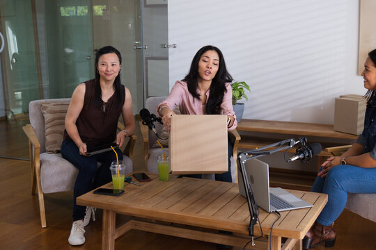 Diverse female creators presenting cardboard box during podcast recording at studio with mics