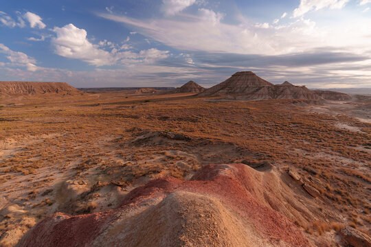 View of the arid, eroded landscape of Bardenas Reales with dramatic rock formations, sparse vegetation, and a vast sky at sunset in Spain.
