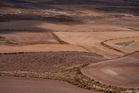 View of arid agricultural fields with terraced land and dirt roads in the dry landscape of Spain.
