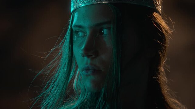 Young Caucasian woman wearing crown turning head with wind blowing hair in extreme close up. Footage suitable for fantasy film trailer, theatrical ad, or cinematic storytelling