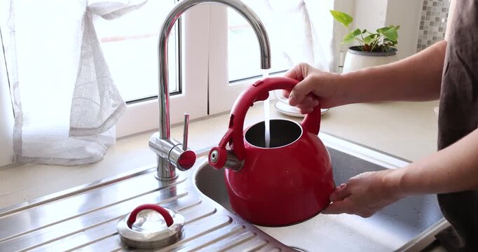 Pouring tap water into red kettle. Modern home resource utility trends. Daily kitchen household chore routine.