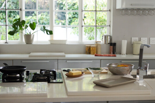 Central kitchen island is showcasing white countertop with gas cooktop, butter, citrus, sunlight