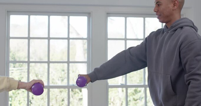 Senior Chinese woman and male guide entering right, raising purple weights, leading home workout