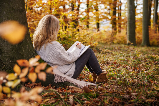Woman sitting in autumn forest writing diary. Journaling for good mental wellbeing and mindfulness intentions