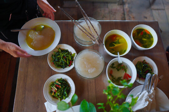 View of a traditional Indonesian meal featuring bowls of papeda, stir-fried water spinach, and various soups served on a wooden table in Indonesia.