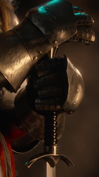 Vertical shot of medieval warrior wearing steel armor gauntlets holding sword hilt. Footage suitable for historical documentary storytelling, fantasy teaser or gaming advertising