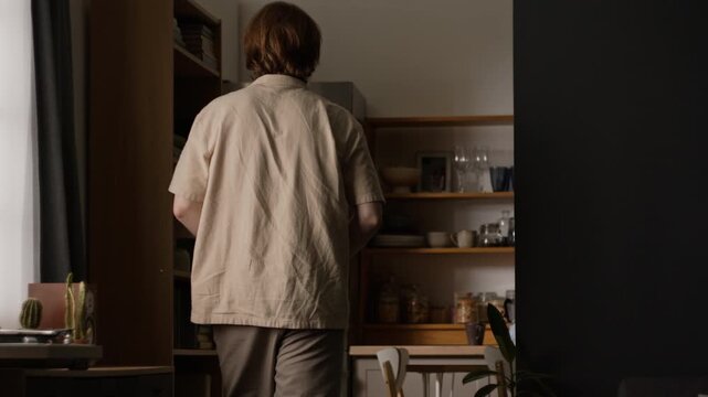 Caucasian young adult man seen from rear view walking, taking glass of water and drinking. Clip suitable for wellness advertising, daily lifestyle projects and healthcare campaigns