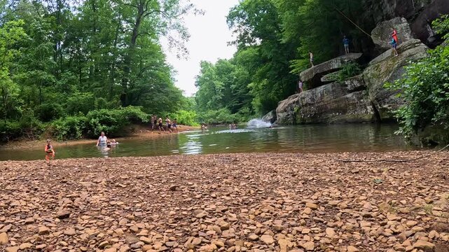 Scenic view of a natural swimming hole at Bell Smith Springs in Shawnee National Forest, Illinois. Highlights visitors swimming, standing along rocky bluffs, and jumping off cliffs into the water.