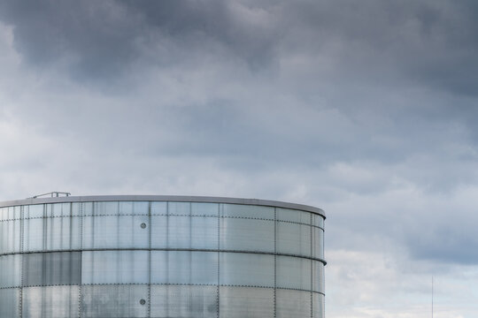View of a large cylindrical metal industrial storage tank against a dramatic overcast sky, Poland.