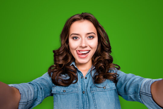 Self-portrait of nice cute stylish trendy flirty cheerful lovely attractive adorable brunette girl with wavy hair in casual denim shirt, showing tongue out, isolated over grey background