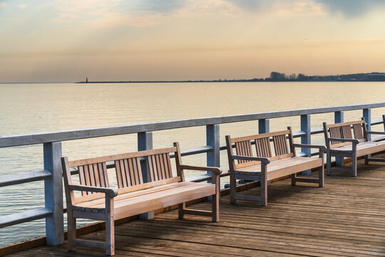 View of wooden benches on the pier overlooking the calm Baltic Sea at sunset in Gdansk, Pomeranian Voivodeship, Poland.