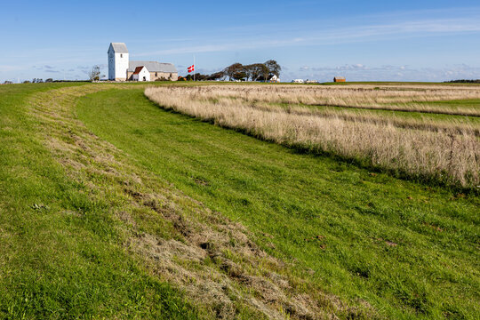 View of the historic Aggersborg Viking ring fortress site featuring a white church and a Danish flag set within expansive green fields in Aggersborg, Jutland, Denmark.