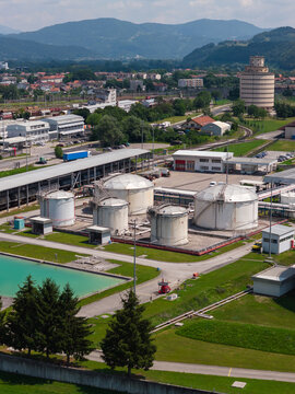 Aerial view shows multiple oil storage tanks at a petroleum facility. Surrounding area includes buildings and green spaces.