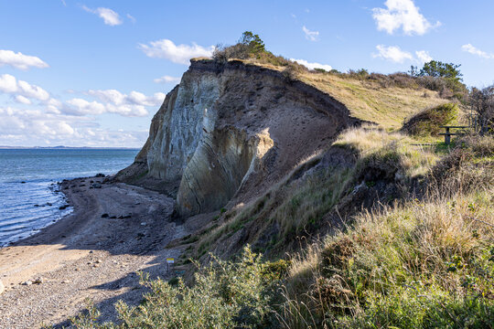 View of the dramatic moler cliffs on the island of Fur, featuring layered geological formations, grassy slopes, and a pebble beach along the coastline in Fur, Jutland, Denmark.