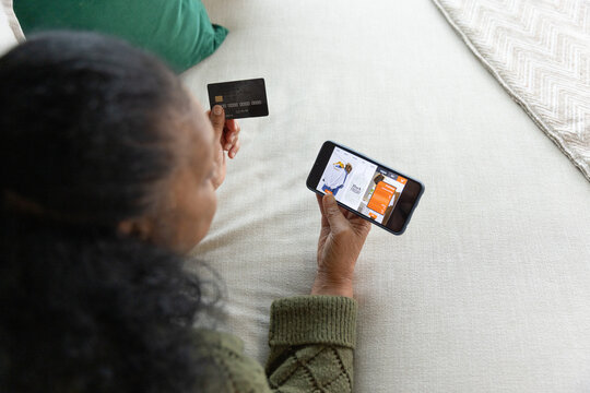 Senior African American woman wearing green sweater holding phone and credit card on bed