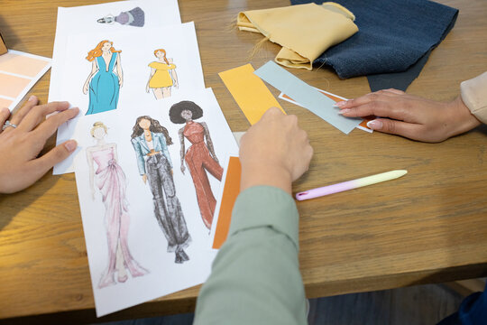 Female team examining sketches, selecting swatches and arranging mustard denim fabric at studio