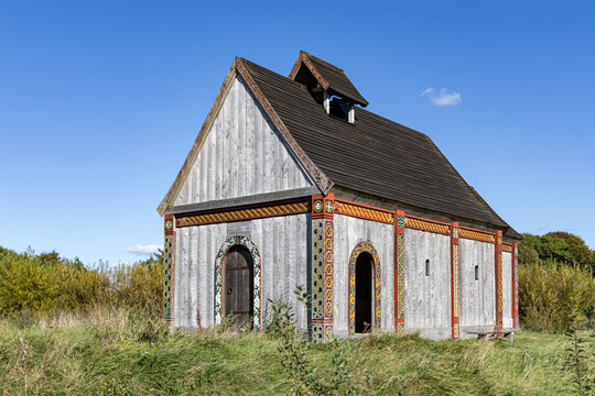View of the reconstructed wooden church at Ribe VikingeCenter with intricate painted patterns on the timber frame, set in a grassy field in Ribe, Jutland, Denmark.