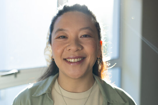 Asian female smiling and standing at bright window wearing light green overshirt, necklace