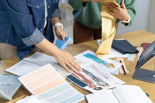 Diverse female designers wearing denim top green knit sorting fabric samples and sketches in studio