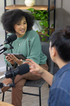African American and Asian women recording in studio holding tablet and mics, green sweater