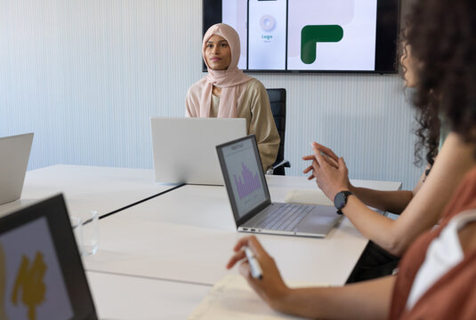 African American women coworkers meeting in conference room, woman in pink hijab using laptop