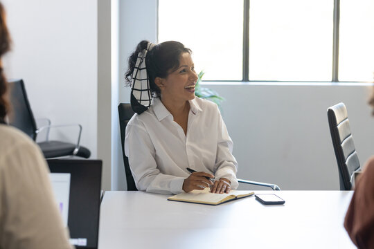 Diverse female coworkers meeting at white table, Indian woman in business wear taking notes, phone