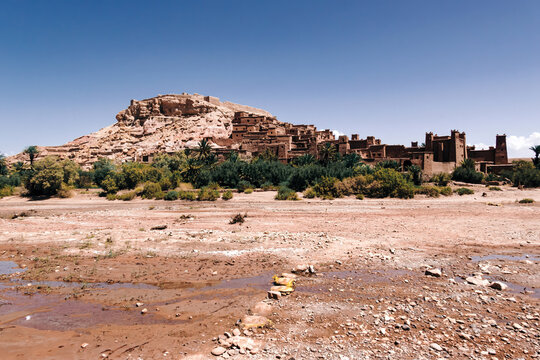 Ait ben haddou, a fortified clay village on a hillside, overlooking a dry riverbed and lush oasis, showcasing traditional berber architecture