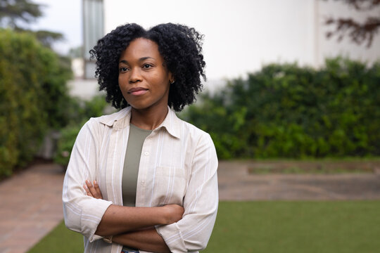 Woman standing in courtyard wearing beige button-up over olive top and small hoop earrings