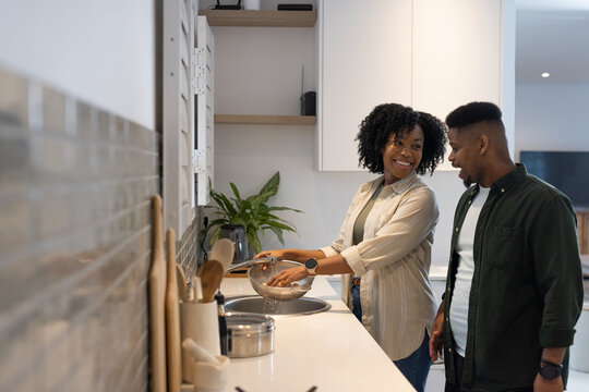 African American couple chatting in kitchen, woman holding metal colander at sink, copy space