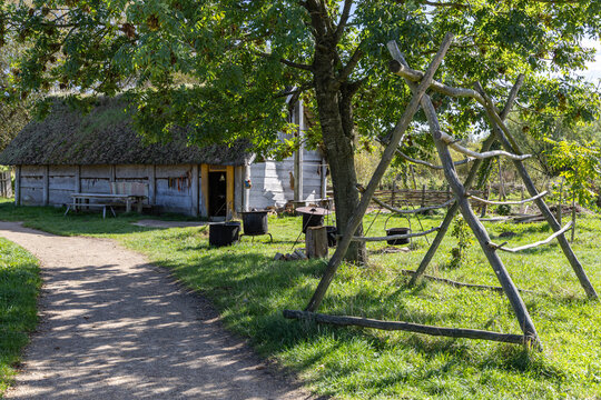 View of the historic Ribe VikingeCenter featuring a traditional wooden house with a thatched roof and an outdoor cooking area with iron pots in Ribe, Jutland, Denmark.