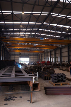 View of a metal fabrication workshop with overhead cranes, steel beams, and welding sparks in an industrial facility in Milan, Lombardy, Italy.