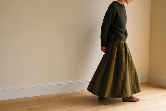 A woman wearing a cozy sweater and a flowing long skirt gracefully walks through a warmly lit room, highlighting her elegant style and comfort in everyday wear.