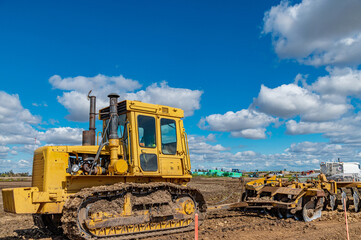 Agricultural view of yellow bulldozer cultivating soil with disc harrow under blue sky. © Todayphoto