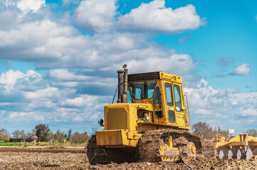Agricultural view of yellow bulldozer cultivating soil with disc harrow under cloudy blue sky. © Todayphoto