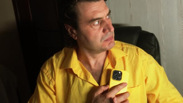 A man is talking on the phone, afraid of being overheard. He is frightened and glances around timidly.