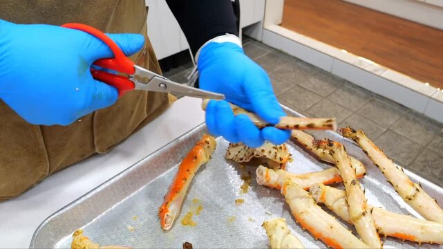 Cutting cooked king crab legs on a metal tray using scissors inside a professional kitchen setting with fresh seafood preparation techniques and gourmet culinary standards