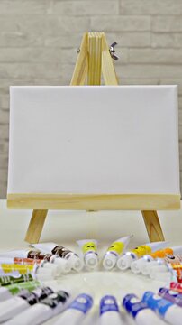 Zooming on mini easel with canvas and color tubes under on table