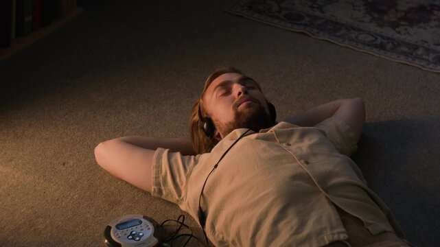 Caucasian young adult man lying on floor, listening to music through headphones with eyes closed from top view. Ideal for mental wellbeing, music streaming service, mindfulness app promotions