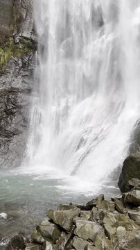 Vertical video of a waterfall ending in a calm river pool.