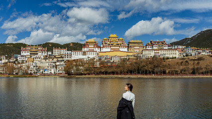 Fototapeta premium Woman gazing at Songzanlin Monastery reflected in the lake, wide view